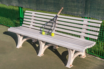 Bench on tennis court with racket and ball