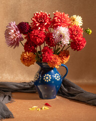 A bright, colorful bouquet of flowers in a blue clay pot on an orange background. Dahlias. The smell of autumn. Calm. Pleasure. Pleasure. Autumn still life.