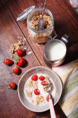 Summer breakfast with granola, fresh srawberry and milk on brown wooden table.