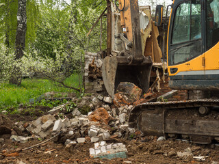 Fototapeta na wymiar Demolition of a building by an industrial yellow excavator. Demolished broken walls a pile of industrial debris