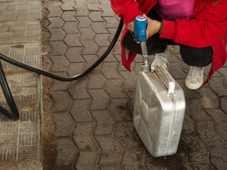 a girl pours gasoline into a metal canister from a pistol at a gas station