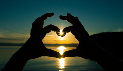 silhouette of a persons hand in the sun, making a heart. Norway