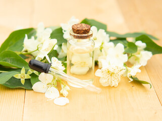 Obraz na płótnie Canvas Jasmine essential oil in a glass bottle on a background of jasmine flowers on a wooden table