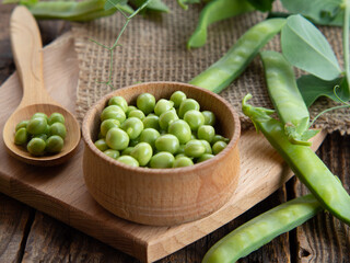 wooden bowl and spoon with fresh peas and their pods on an old wooden table, rustic background with peas