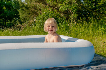 Cute adorable little toddler kid boy having fun playing in inflatable pool on private house...