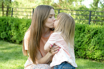 People. A family. Mom and daughter hug and kiss tightly in the park in summer.