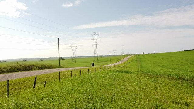 Tracking motion of adventure motorcycle riders travelling fast down a county gravel road with Transmission towers and power poles on the Canadian Prairies.