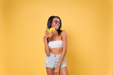 Fototapeta na wymiar happy African American woman dressed in summer clothes drinking a cocktail on a hot summer day isolated over yellow background