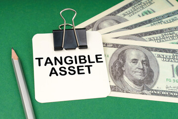 On a green surface, a pen, dollars and paper with the inscription - Tangible Asset