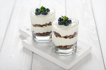 Dessert with cottage cheese, fresh blueberries and granola in a glass on a white wooden background.
