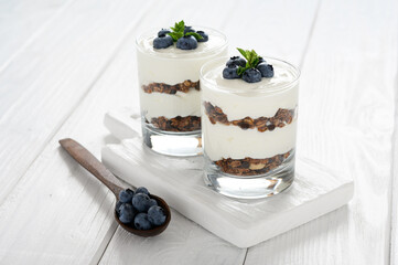 Dessert with cottage cheese, fresh blueberries and granola in a glass on a white wooden background.