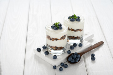 Dessert with cottage cheese, fresh blueberries and granola in a glass on a white wooden background.