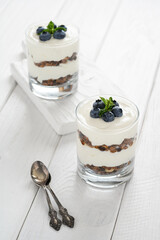 Dessert with cottage cheese, fresh blueberries and granola in a glass on a white wooden background.