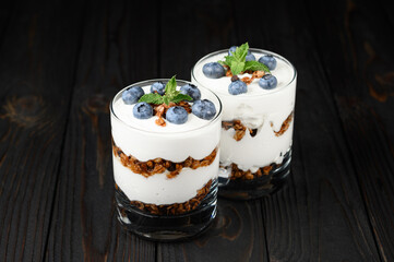 Homemade layered dessert with fresh blueberries, cream cheese or yogurt, granola on rustic background.