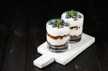 Homemade layered dessert with fresh blueberries, cream cheese or yogurt, granola on rustic background.