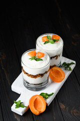 Homemade layered dessert with fresh apricot, cream cheese or yogurt, granola on rustic background.
