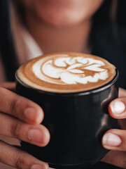 Coffee shop heart cream design on black mug in hands. Hot coffee espresso barista latte art. Relaxing space with coffee in hands	