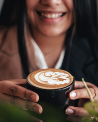 Smiley face - Coffee shop heart cream design on black mug in hands. Hot coffee espresso barista latte art. Relaxing space with coffee in hands	