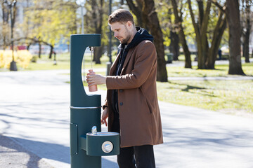 Man refilling his water bottle at the city. Free public water bottle refill station. Sustainable...