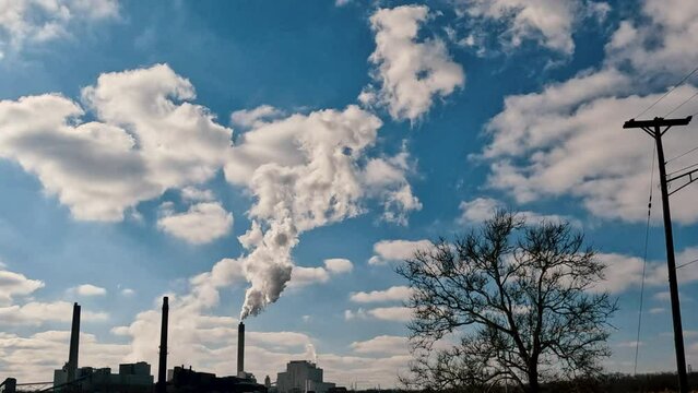 Coal-fired power station emitting a plume of particulate smoke up into the clouds. Bright blue winter sky in the background. Slight slow motion.