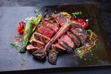 Traditional barbecue dry aged wagyu porterhouse beef steak bistecca alla Fiorentina with grilled vegetable and spice sliced and served as close-up on an old rustic board
