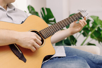 Close-up of a man's hands playing an acoustic guitar while sitting on the couch at home. Calm rest at home. Learning to play a musical instrument.