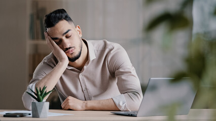 Tired sleepy hispanic man arab guy dreaming overworked male student slumber at office laying down...