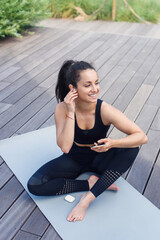Woman lying on yoga mat after exercising, relaxing with smartphone and listening to music. Workout Playlist.