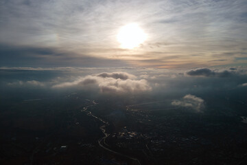 Aerial view from high altitude of distant city covered with puffy cumulus clouds flying by before...