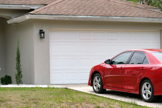 Car Parked In Front Of Wide Garage Double Door On Concrete Driveway Of New Modern American House