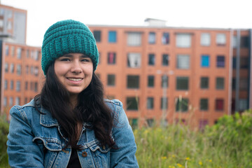 Woman smiling in a green area against a backdrop of apartments.