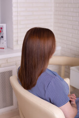 Female back with long straight brunette hair in hairdressing salon
