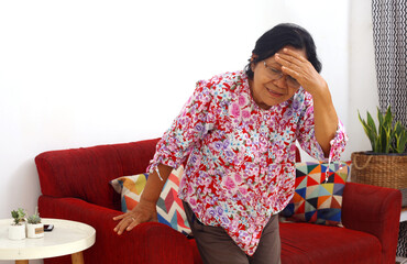 Senior asian woman with headache or dizzy or migraine when will stand from sofa at home.