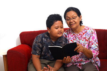Front view of an Asian grandmother and her grandson reading a story book in living room at home