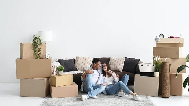 Moving to new apartment, buying home. Happy young multiracial couple, caucasian woman and hispanic guy, are sitting in their new home on the floor between boxes of stuff, planning their house design