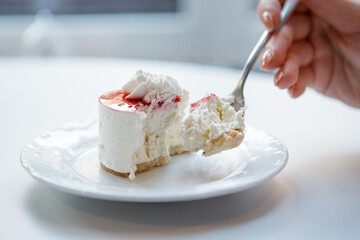 Red and white cake being cut with fork in female hand.