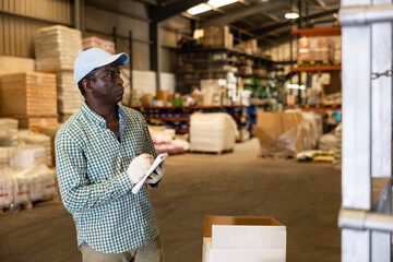 Portrait of focused African-American man checking order list at warehouse
