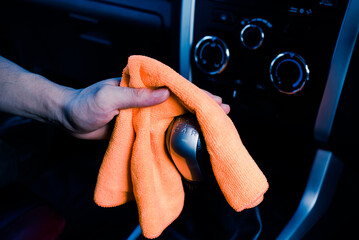 Hand cleaning the car interior with orange microfiber cloth