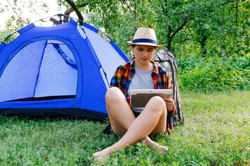 Defocus young woman working on tablet near camping tent outdoors surrounded by beautiful nature....