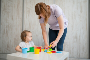 Obraz premium One girl small caucasian toddler child playing with colorful plasticine on the table at home with her mother woman childhood and growing up development concept copy space