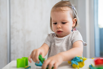 One girl small caucasian toddler child playing with colorful plasticine on the table at home alone childhood and growing up development concept copy space