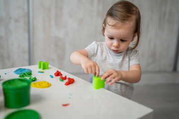 Fototapeta na wymiar One girl small caucasian toddler child playing with colorful plasticine on the table at home alone childhood and growing up development concept copy space