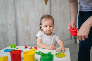 One girl small caucasian toddler child playing with colorful plasticine on the table at home alone childhood and growing up development concept copy space