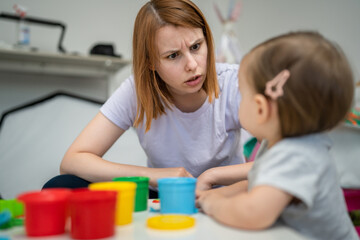 One girl small caucasian toddler child playing with colorful plasticine on the table at home with her mother woman talking angry mad childhood and growing up development concept copy space side view