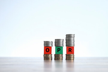Word OPR on the wooden blocks sandwiched between stacked coins on white background