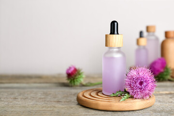 Bottle of essential oil and flower on wooden table. Space for text