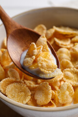 Spoon with tasty cornflakes and milk over bowl, closeup