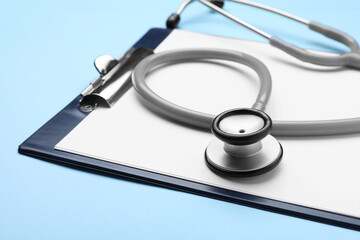 Stethoscope and clipboard on light blue background, closeup