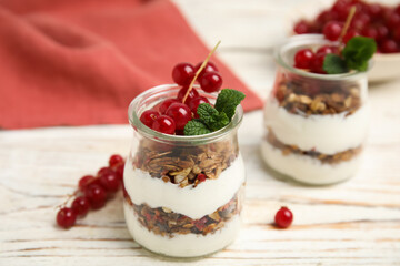 Delicious yogurt parfait with fresh red currants and mint on white wooden table, closeup