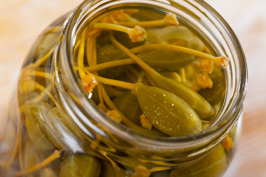 Closeup of glass jar with pickled green capers on a wooden background